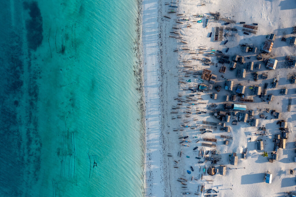 Aerial view of a beach with wooden homes and boats on the shore