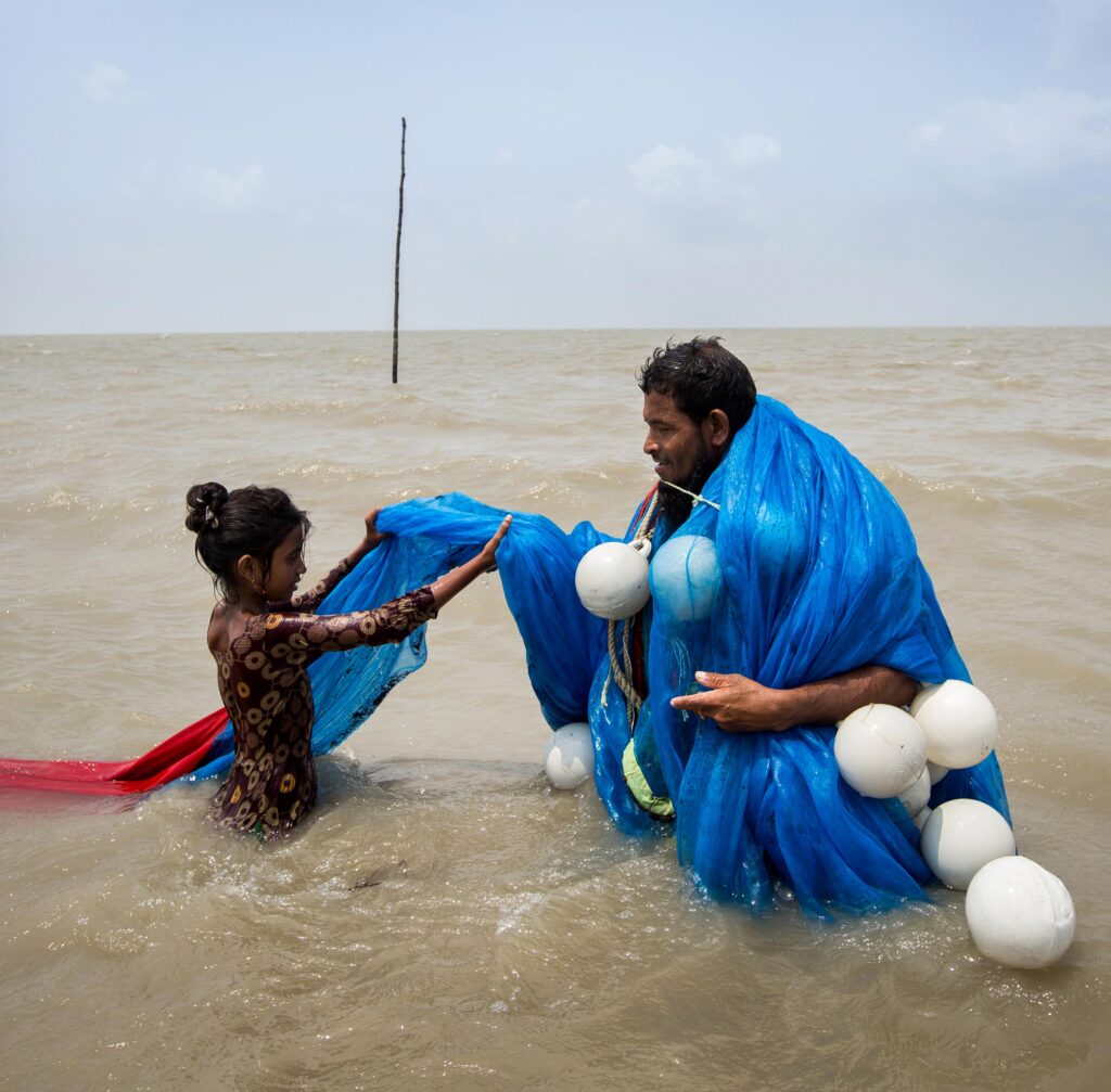 Father and daughter standing in the ocean holding a blue net with buoys