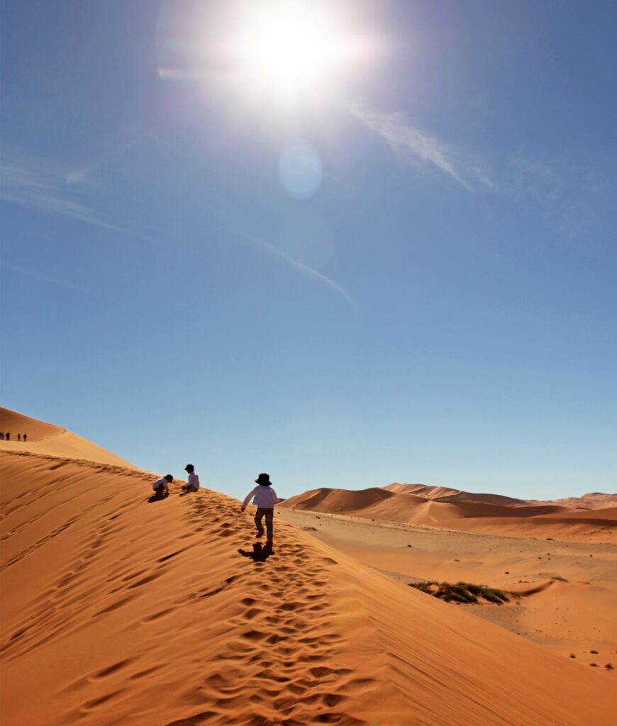 children walking on sand dune with a bright sun in a blue sly